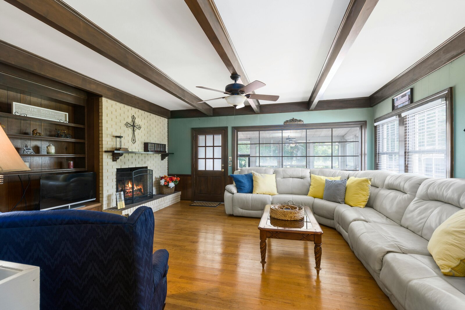 A warmly lit living room with a fireplace, sectional sofa, and exposed wood beams